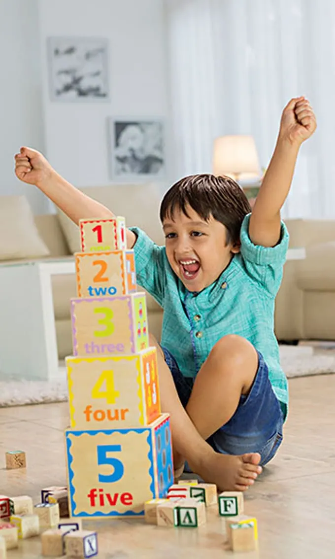 Excited young boy playing with stacked number blocks